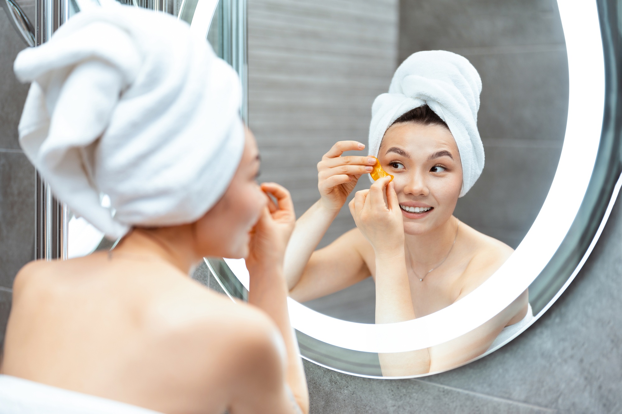 Young Woman Applying Skin Care Products In Mirror